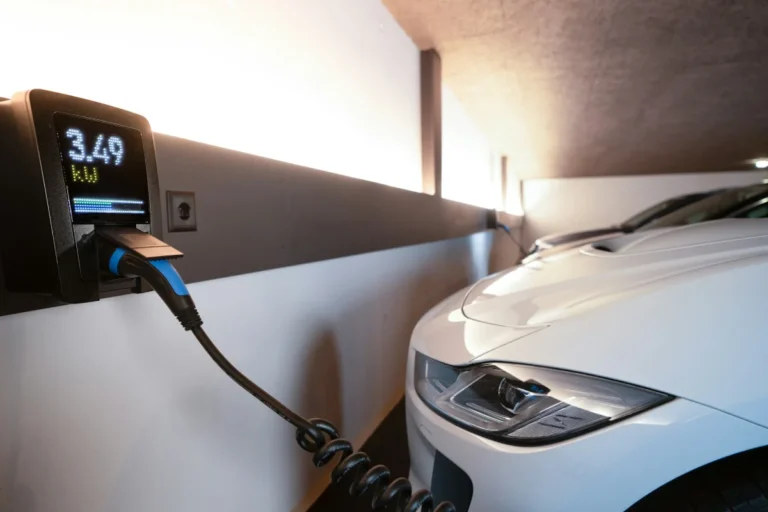 A modern white electric vehicle plugged into a wall-mounted Level 2 home charging station, representing the residential equipment that qualifies for the Section 30C federal tax credit.