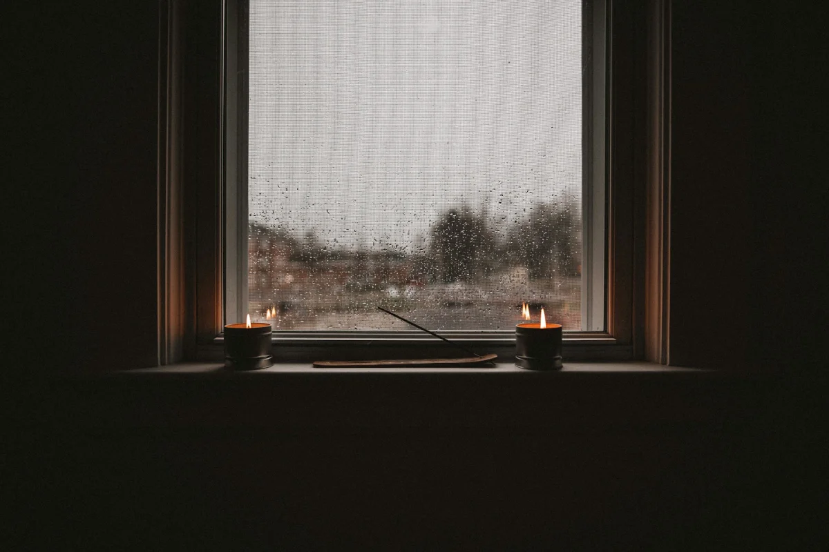 Two lit candles on a white window sill during a rainy evening, illustrating the transition to a modern residential backup power system for reliable home lighting.