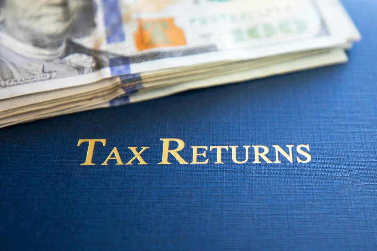 A close-up of a folder labeled Tax Returns with U.S. dollar bills, illustrating the financial impact of the 2026 federal energy tax credits and OBBB Act incentives.